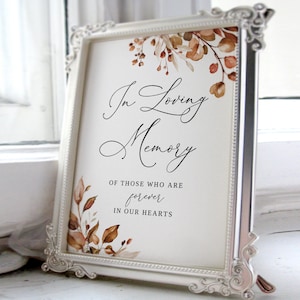 May include: A white framed sign with a watercolour floral design in shades of brown and orange. The sign reads "In Loving Memory" and "Of those who are forever in our hearts".