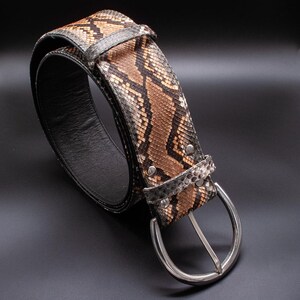 May include: A brown and black snakeskin belt with a silver buckle. The belt is made of genuine leather and has a classic design.