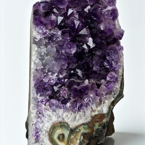 May include: A striking amethyst geode, showcasing a cluster of deep purple crystals. The base displays a mix of colours, including brown, green, and white. The crystal formations are well-defined and catch the light.