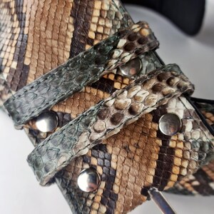 May include: A brown, black and green snakeskin belt with a silver buckle. The belt has a textured pattern and is made of real leather.
