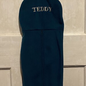 Peut inclure: Un sac &agrave; bottes en polaire bleu sarcelle avec une boucle de suspension noire et le nom "TEDDY" brod&eacute; en blanc sur le devant.