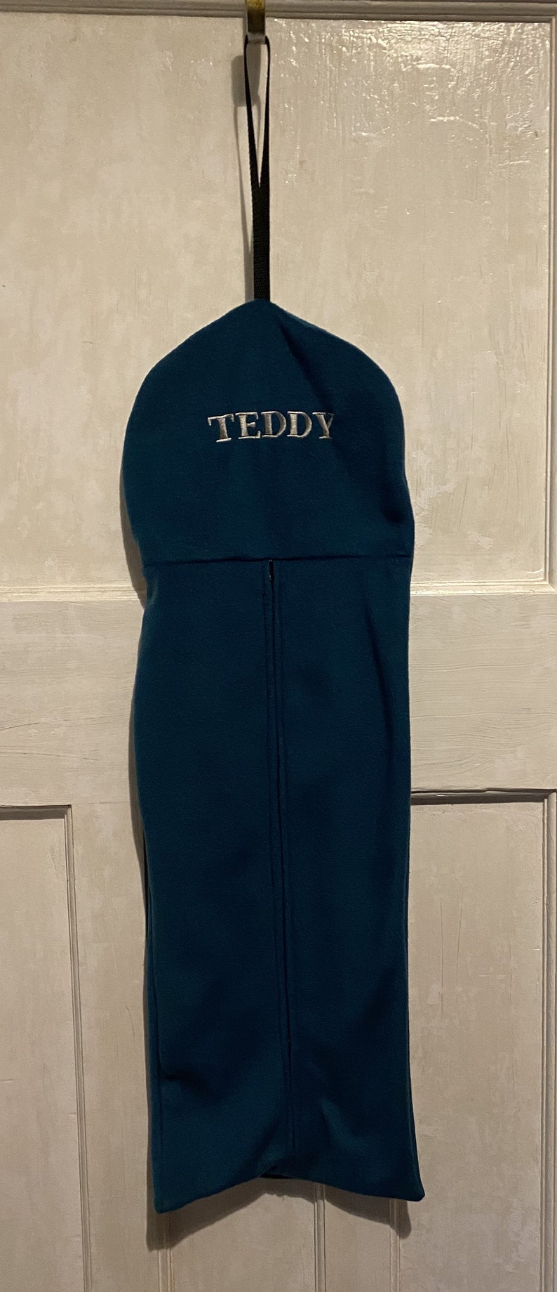 Peut inclure: Un sac &agrave; bottes en polaire bleu sarcelle avec une boucle de suspension noire et le nom "TEDDY" brod&eacute; en blanc sur le devant.