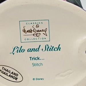 May include: A ceramic figurine base with the text "Lilo and Stitch" and "Trick... Stitch." The base also features the "Classics Collection" logo and the Disney logo. The figurine is made in Thailand.