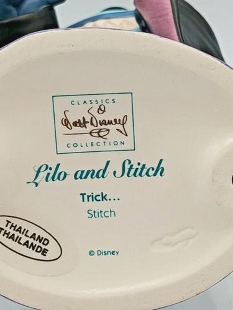 May include: A ceramic figurine base with the text "Lilo and Stitch" and "Trick... Stitch." The base also features the "Classics Collection" logo and the Disney logo. The figurine is made in Thailand.
