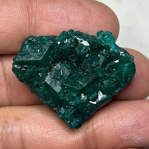 Könnte beinhalten: Ein rohes, tief smaragdgrünes Mineralexemplar, das aus einer Ansammlung kantiger, kristalliner Strukturen mit einer reflektierenden, facettierten Oberfläche besteht. Der Stein zeigt eine satte, gesättigte Farbe und eine gezackte, unregelmäßige Form.