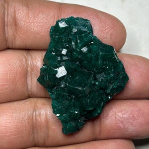Könnte beinhalten: Eine Ansammlung tiefgrüner, smaragdgrüner Kristalle mit einer gezackten, facettierten Oberfläche. Das Mineralexemplar weist zahlreiche kleine, scharfe, würfelartige Formationen auf, die das Licht reflektieren und eine Textur erzeugen.