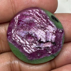Peut inclure: Une pierre précieuse polie de forme circulaire présentant un centre magenta et violet profond vibrant avec une bordure verte opaque, lisse et distincte. La surface offre un aspect cristallin texturé avec des fractures internes visibles.