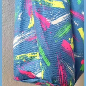 May include: A blue fabric bag featuring a textured, woven surface pattern with diagonal brushstroke designs in vibrant neon pink, bright lime green, and stark white colors, showcasing a repeating abstract paint splatter aesthetic throughout.