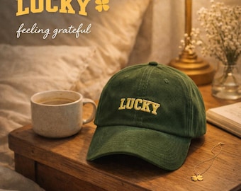Peut inclure: Casquette de baseball en velours côtelé vert avec le mot "LUCKY" brodé en or. L'image comprend également une tasse à café, un collier en or et le texte "LUCKY feeling grateful".