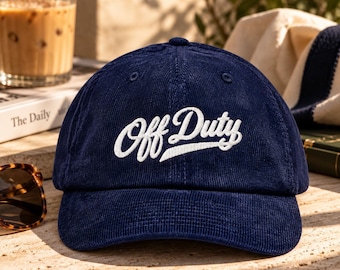 Peut inclure: Une casquette de baseball en velours côtelé bleu marine avec le texte Off Duty brodé en blanc dans une police cursive sur les panneaux avant. La casquette présente une calotte structurée, une visière incurvée et des coutures bleu marine.