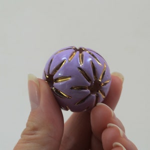 Könnte beinhalten: Eine violette Kugel mit einem goldenen Sternmuster. Die Kugel ist etwa so groß wie ein Golfball.