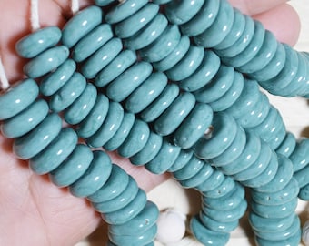 May include: A strand of turquoise blue ceramic beads, each bead is a donut shape with a hole in the center. The beads are strung on a white cord.