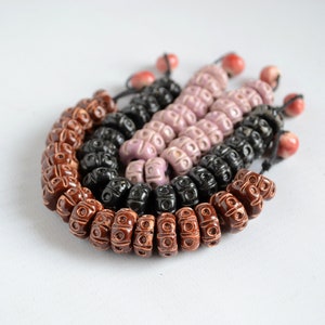 May include: A set of three ceramic bead necklaces in brown, black, and pink. The beads are all round and have a textured surface. The necklaces are strung on a thin cord.