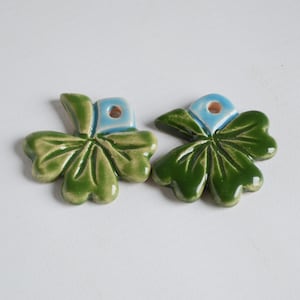 May include: Two green four-leaf clover charms with blue centers and a hole for hanging.