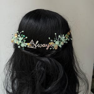 Puede incluir: Un peine de pelo plateado con cuentas verdes y doradas y la palabra "Always" en cursiva. El peine está decorado con un pequeño símbolo triangular.