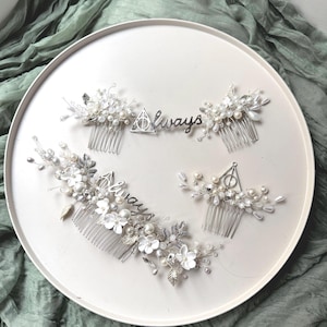 May include: Four silver hair combs with white pearl and flower embellishments. The combs feature a silver triangle symbol and the word "Always".