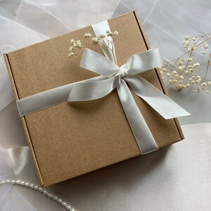 May include: A brown cardboard gift box with a white satin ribbon tied in a bow. The box is decorated with small white flowers.