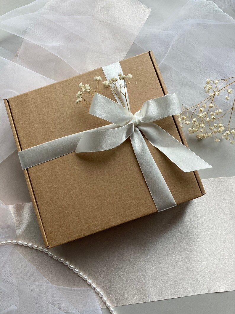 May include: A brown cardboard gift box with a white satin ribbon tied in a bow. The box is decorated with small white flowers.