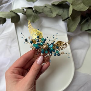 Può includere: Pettine per capelli dorato con un paio di ali e perline blu e bianche.