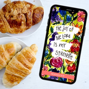 May include: A phone screen with a floral background and the text "The joy of the Lord is my strength. Nehemiah 8:10".