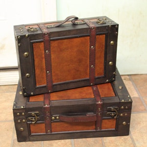 May include: Two vintage-style brown leather suitcases with brass accents and buckles. The suitcases are stacked on top of each other.
