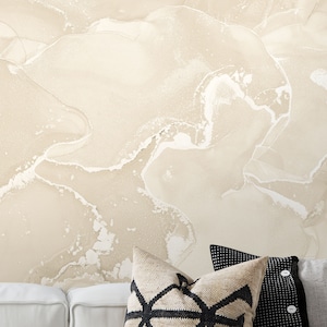 Puede incluir: Una impresión de acuarela abstracta beige y blanca con un sutil efecto marmoleado. La impresión se muestra en un sofá blanco con almohadas de tiro con patrones en blanco y negro.