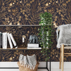 May include: A dark blue wallpaper with a gold floral pattern. The wallpaper features a variety of botanical illustrations, including ferns, leaves, and flowers. The wallpaper is displayed in a room with a shelf, a plant, and a chair.