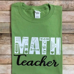 May include: Green t-shirt with the word "MATH" in white letters with math symbols inside each letter. The word "Teacher" is in black below the word "MATH".