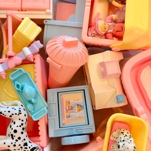 May include: A collection of miniature plastic dollhouse furniture and accessories in pastel colors, including a television with a screen image, a pink trash can, a blue tea set, a yellow bed with dalmatian figures, and small dolls in a yellow cradle.
