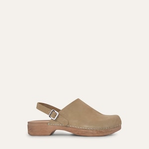 Può includere: Zoccolo color beige con suola in legno e cinturino alla caviglia. La scarpa ha una chiusura con fibbia e una punta arrotondata. La tomaia è in materiale simile alla pelle scamosciata. La suola in legno è alta circa 5 cm.