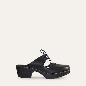 May include: Black leather clogs with a rounded toe and a small heel. The clogs have a lace-up detail and decorative cutouts on the top. The sole is dark brown with a white stitch detail.