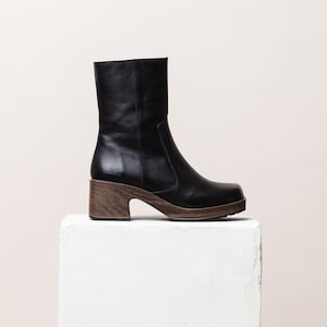 May include: Black leather ankle boots with a chunky wooden heel. The boots have a square toe and a zipper on the back.