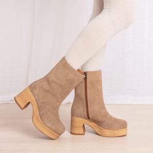 May include: Tan suede ankle boots with wooden platform soles and heels. The boots have a side zipper and a rounded toe. The platform sole measures approximately 2 inches, and the heel is about 4 inches high.