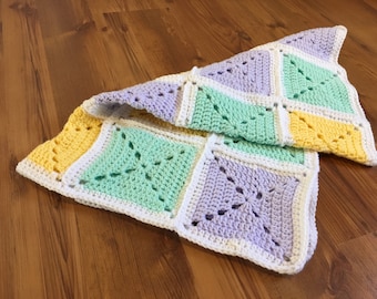 May include: A crocheted baby blanket with a patchwork design in shades of yellow, green, purple, and white.