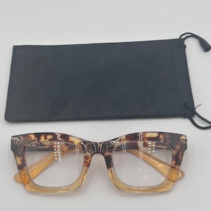 Puede incluir: Gafas de montura cuadrada con un patrón de carey en la parte superior de la montura y las patillas, que se transforma en un color ámbar claro hacia la parte inferior. Se incluye una funda negra con cordón.