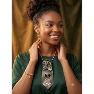 Puede incluir: Una corbata verde oscuro con patrón de puntos, adornada con un emblema de corona dorada, un gráfico de una persona con afro y el texto "QUEEN" y "Health & Fitness". La corbata se lleva con una cadena dorada, pendientes de aro y una pulsera.