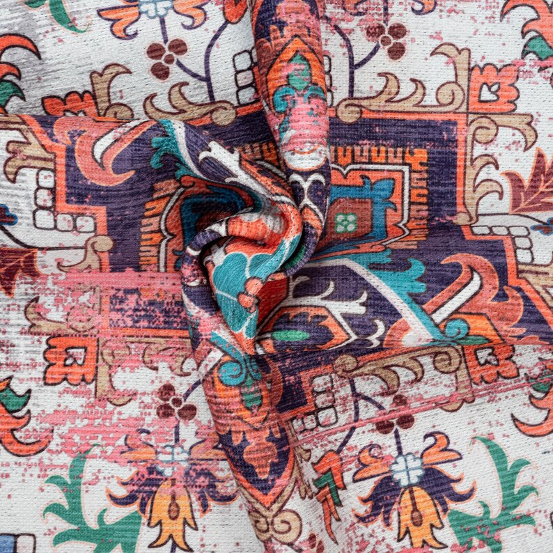 Puede incluir: Primer plano de una tela doblada con un patr&oacute;n ornamentado y desgastado. El dise&ntilde;o presenta una mezcla de colores, incluyendo naranja, turquesa, morado y rosa, sobre un fondo blanco. El patr&oacute;n se asemeja a una alfombra o tapiz tradicional.