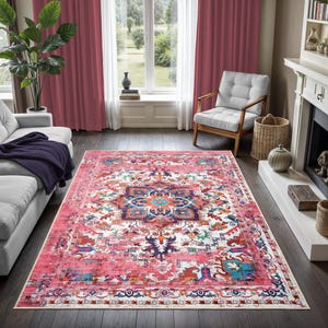 Puede incluir: Una alfombra rectangular grande con un aspecto vintage y desgastado. La alfombra presenta un dise&ntilde;o de medall&oacute;n central en tonos de azul, naranja y turquesa, sobre un fondo rosa y blanco. La alfombra est&aacute; colocada sobre un suelo de madera oscura.