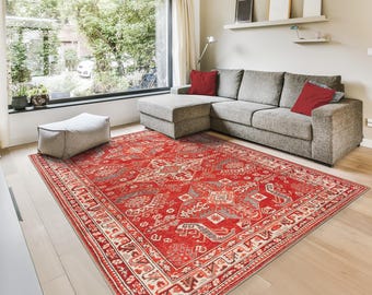 May include: A large, rectangular red rug with an intricate, geometric pattern dominates the room. The rug features a central design with repeating shapes in shades of red, gray, and cream. The rug is placed on a light-colored wooden floor.