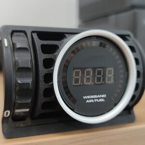 May include: A black wideband air fuel gauge with a white bezel and a digital display showing 8.8.8. The gauge has a knob on the side.