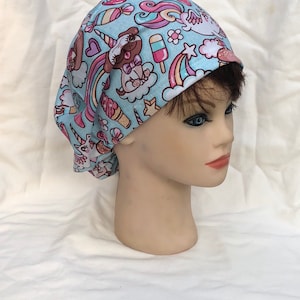 May include: A light blue surgical scrub hat with a colorful print of unicorns, rainbows, ice cream cones, and a dog wearing a bow tie.