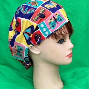 May include: A colorful surgical scrub cap featuring a patchwork design with butterflies, bees, and floral elements. The cap's pattern includes squares of red, yellow, blue, and pink, creating a vibrant and eye-catching accessory.