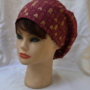 May include: A burgundy scrub hat with a gold arrow pattern. The hat is made of soft, comfortable fabric and is perfect for nurses, doctors, and other healthcare professionals.