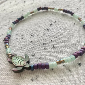 May include: A purple and green beaded bracelet with a silver turtle charm.