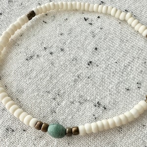 May include: A white beaded bracelet with a single teal bead and gold accents.