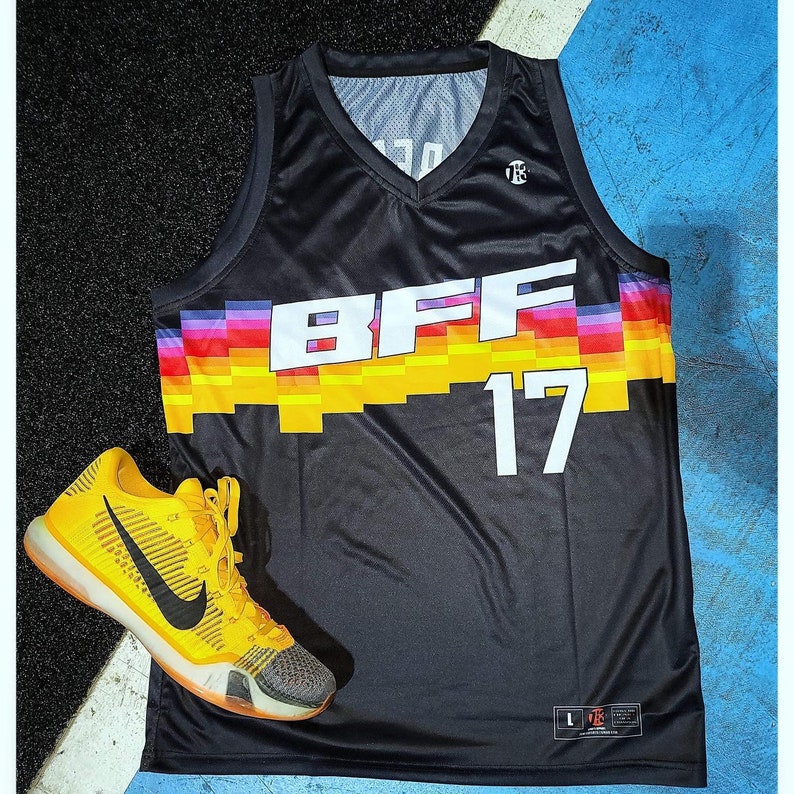 Puede incluir: Camiseta de baloncesto negra con un dise&ntilde;o de rayas arco&iacute;ris y el texto "BFF 17". Una zapatilla de baloncesto amarilla y negra est&aacute; en primer plano.