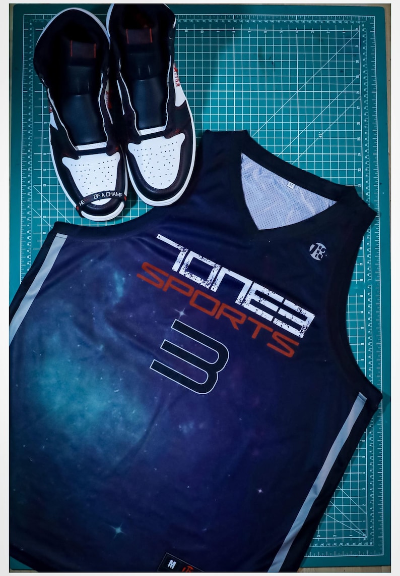 Puede incluir: Una camiseta de baloncesto negra con estampado de galaxia y el texto "Toney Sports 3" en blanco y rojo. La camiseta tiene un ribete blanco alrededor del cuello y las sisas.