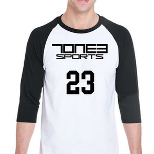 Puede incluir: Una camiseta de béisbol blanca y negra con el texto "JONES SPORTS" y el número "23" impreso en la parte delantera.