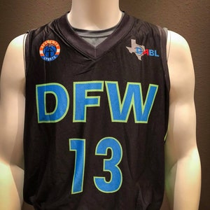 Puede incluir: Camiseta de baloncesto negra con un "DFW 13" verde y azul en la parte delantera. La camiseta tiene un peque&ntilde;o logotipo en el lado izquierdo que dice "Apogee Sports" y un logotipo m&aacute;s grande en el lado derecho que dice "D-ABL" con un contorno de Texas.