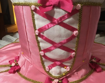 May include: A pink and white ballet tutu with a pink ribbon bow and gold trim. The bodice is decorated with pink roses and a criss-cross ribbon lacing.